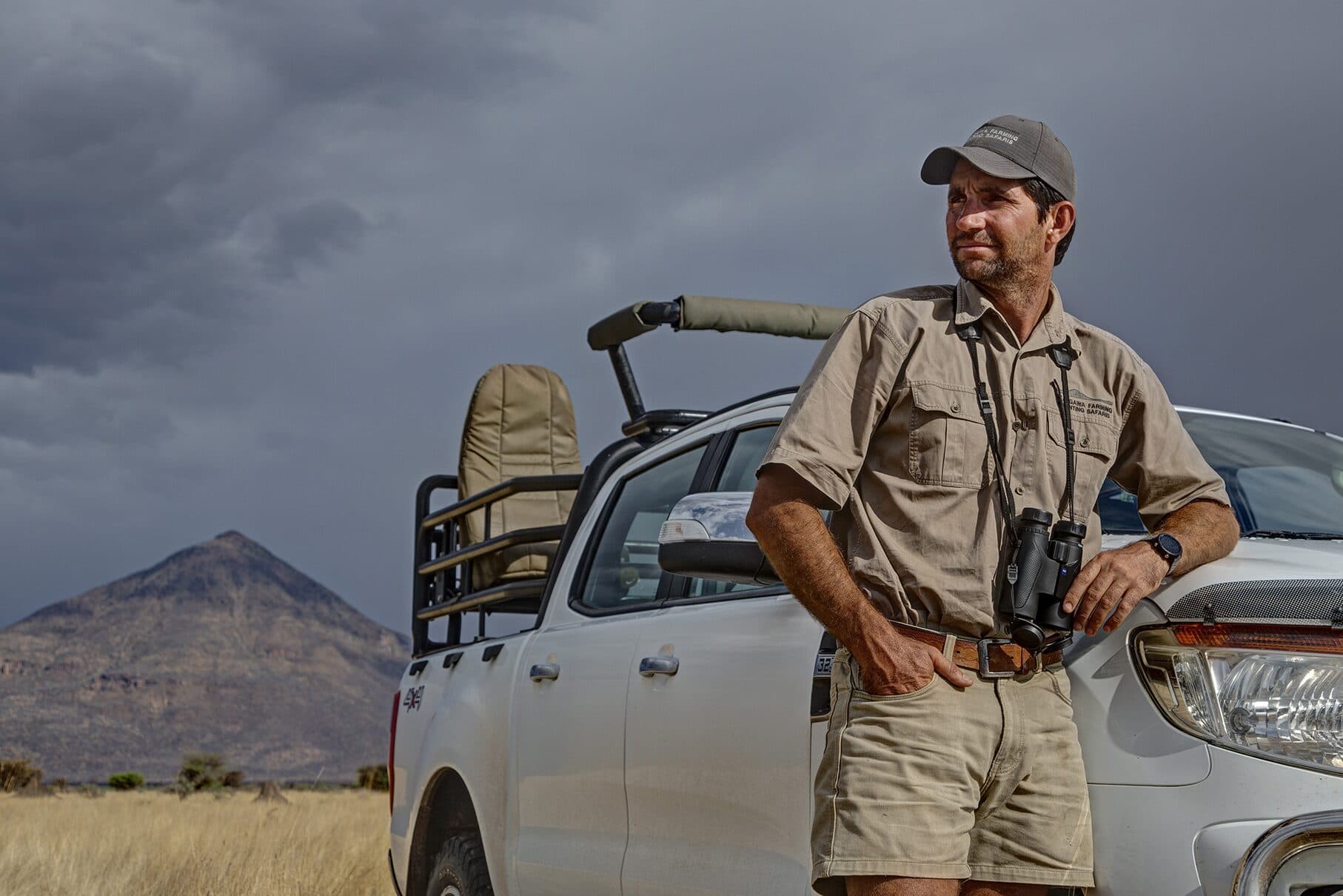 Andrew Campbell with binoculars beside the hunting vehicle