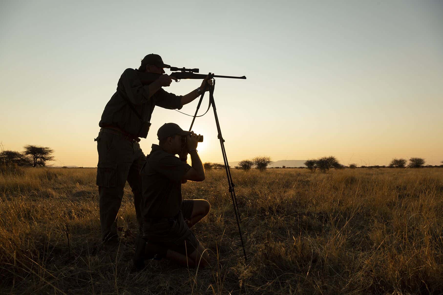 A hunter on shooting sticks with his guide glassing beside him at sunset